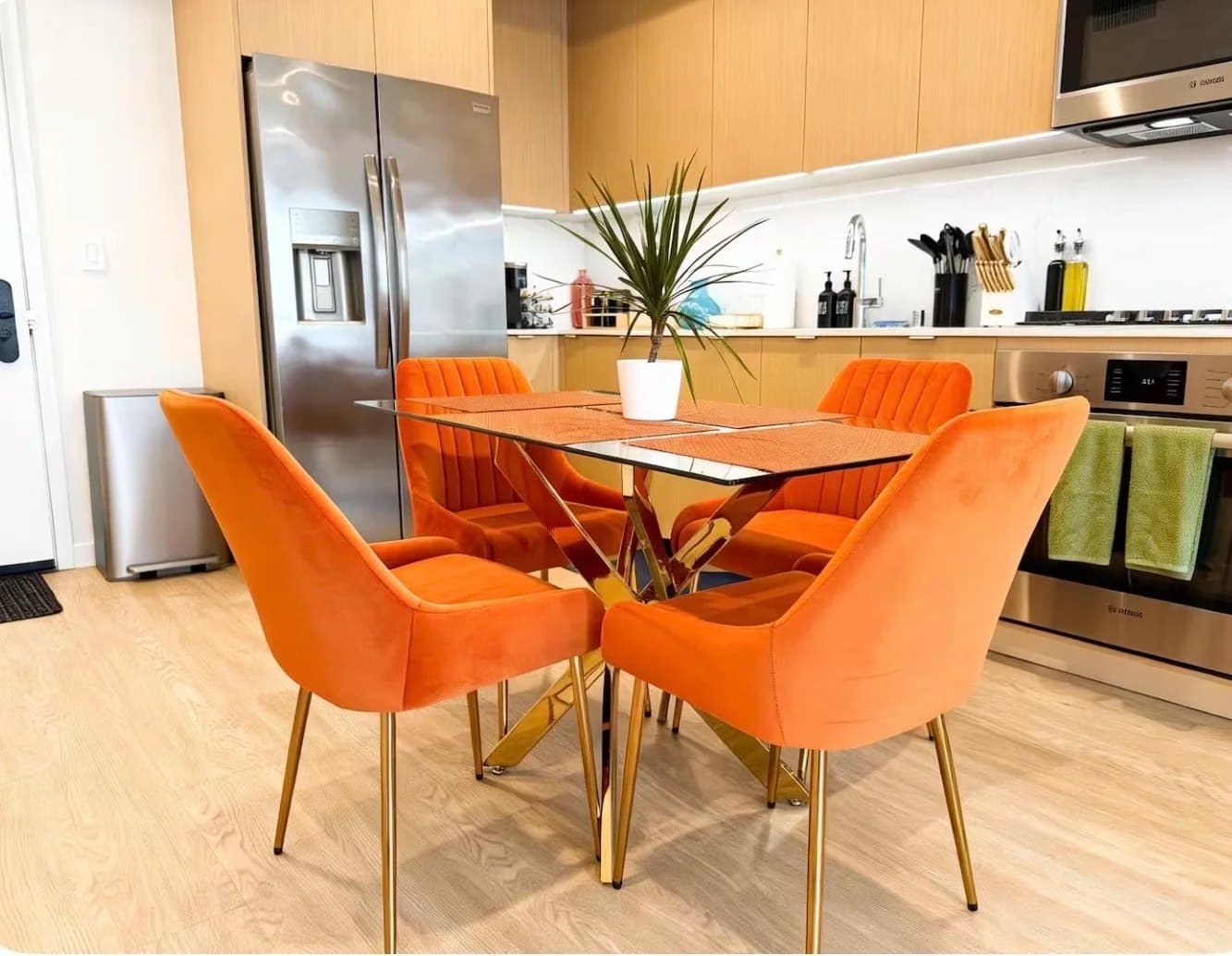 Dining area with glass table and four orange velvet chairs beside a modern furnished kitchen