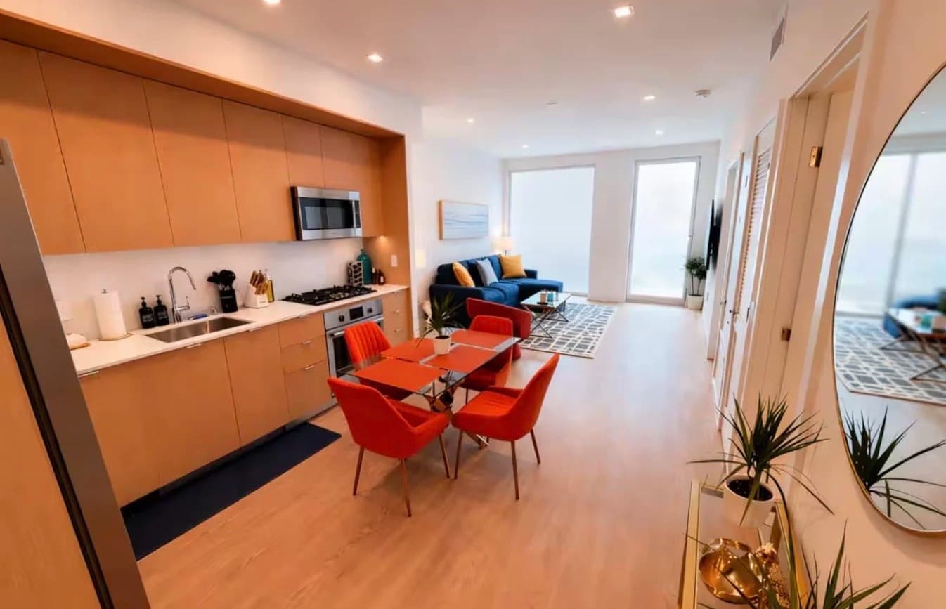 Open-plan living, kitchen and dining area with navy sofa, orange dining set and balcony doors in a Santa Monica rental