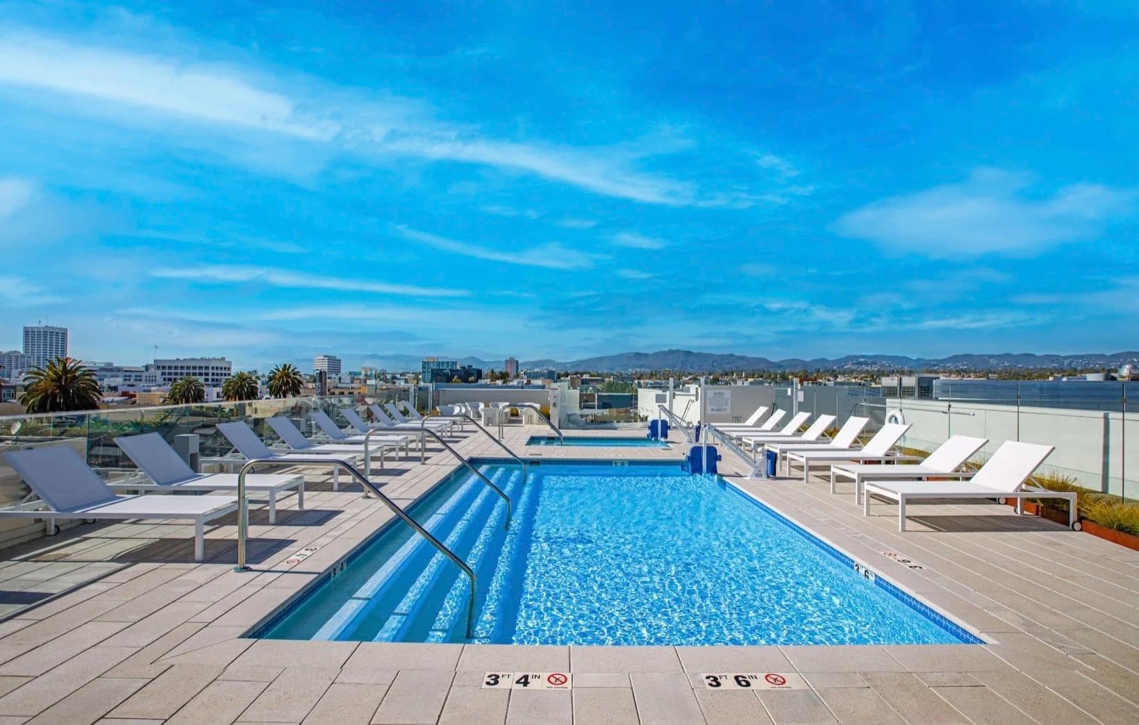 Rooftop pool with lounge chairs and Santa Monica city and mountain views
