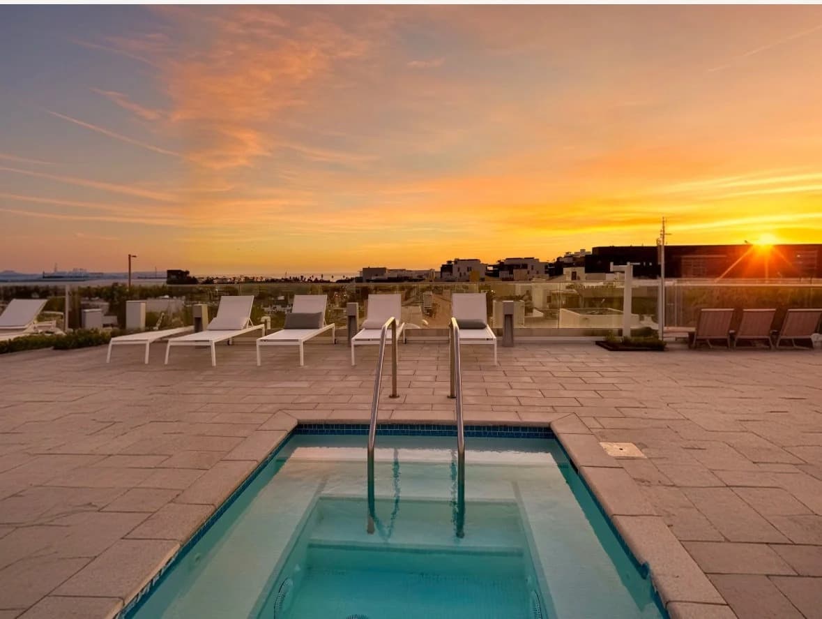 Rooftop spa pool and lounge chairs with city and ocean views at sunset at a Santa Monica building