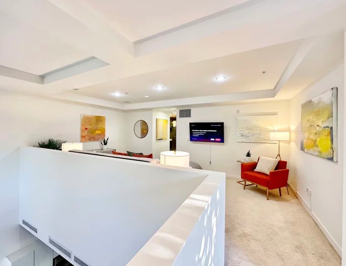 Furnished living room with tray ceiling, orange accent chair, wall-mounted TV and abstract art in a Santa Monica monthly rental
